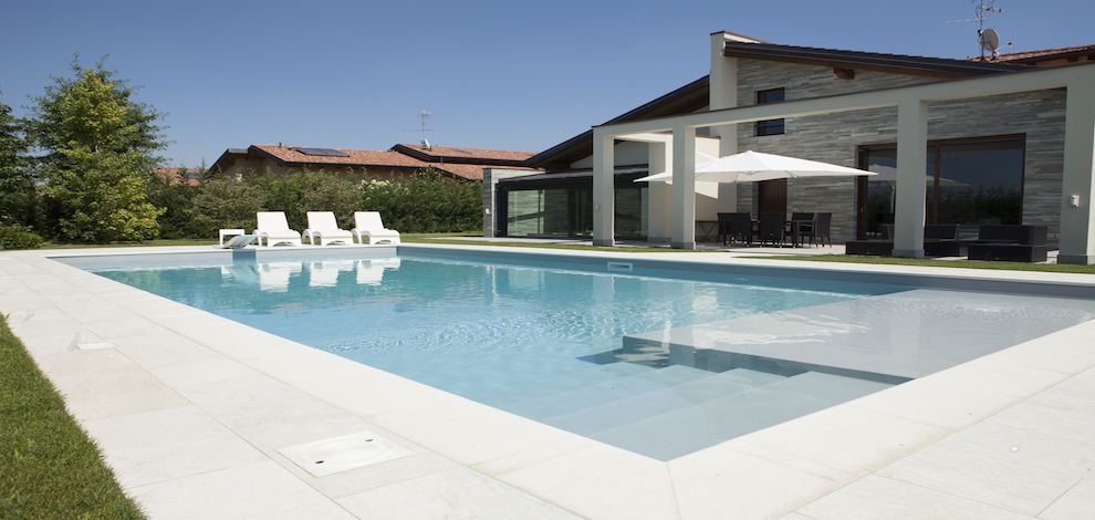 Piscina con bordo chiaro e scala a gradoni davanti a una villa moderna